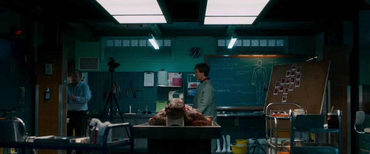 The Autopsy of Jane Doe (2016) movie still: wide — A sterile laboratory or autopsy room features tiled walls, a chalkboard, and metal equipment. Two…
