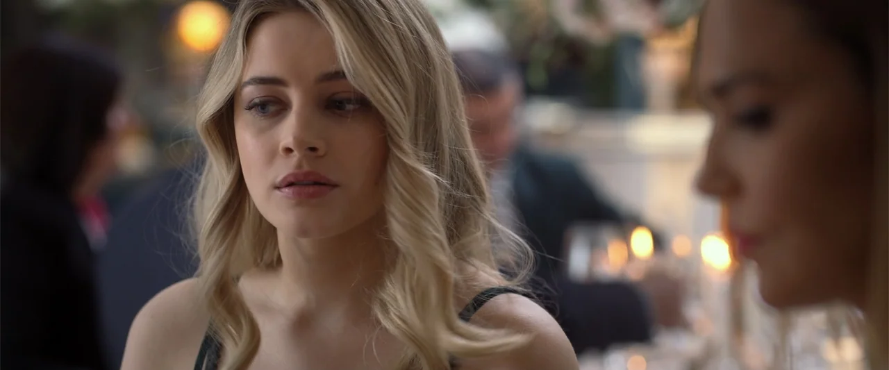 After Ever Happy (2022) movie still: closeup — A dimly lit indoor space features blurred warm light sources in the background. A young blonde woman…