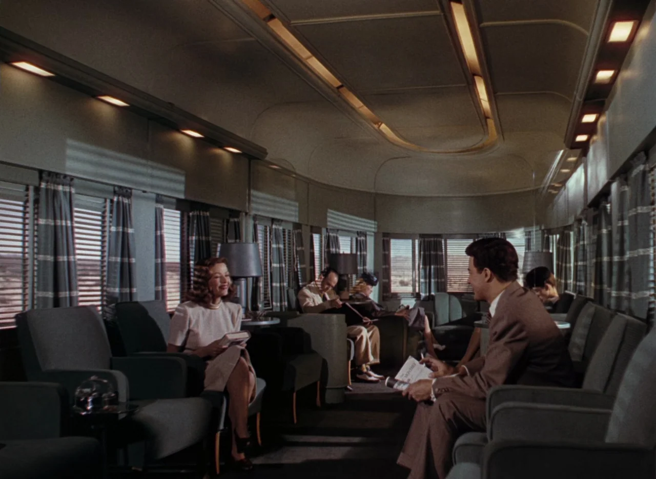 Leave Her To Heaven (1945) movie still: wide — A mid-century modern train passenger car with upholstered chairs and a curved ceiling. A man and a…
