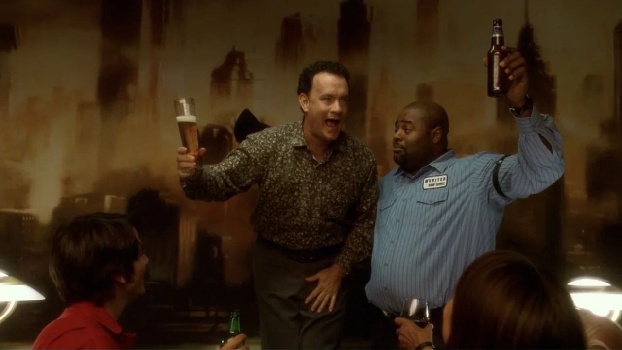 The Terminal (2004) movie still: medium — A dimly lit bar features a mural-covered wall with blurred architectural shapes. Two men stand together…