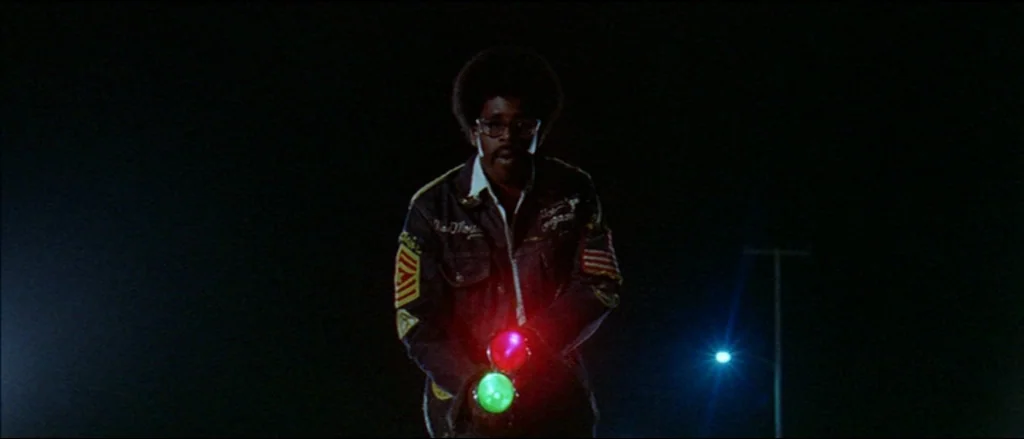 Two Lane Blacktop (1971) movie still: medium — A dark, empty road at night provides a backdrop for a man with glowing items. The man stares forward…