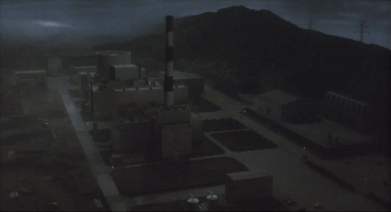 The Return of Godzilla (1984) movie still: establishing — A high-angle view of a sprawling industrial nuclear power plant at night. The complex…