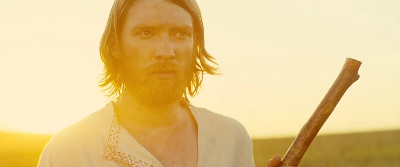 Anna Karenina (2012) movie still: medium — A vast open field at sunset bathed in golden light. A man in a plain tunic holds a wooden staff.