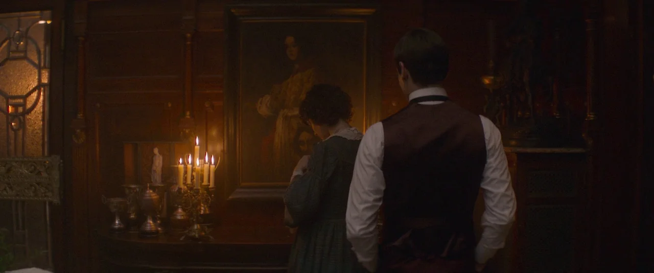 The Dancer movie still: medium — A dimly lit room features dark wood paneling and a large framed portrait. A man in a waistcoat and a woman in a…