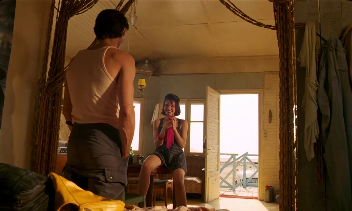 Betty Blue (1986) movie still: medium — An interior space framed by draped fabric leads to a bright, sunlit coastal doorway. A man in a tank top…