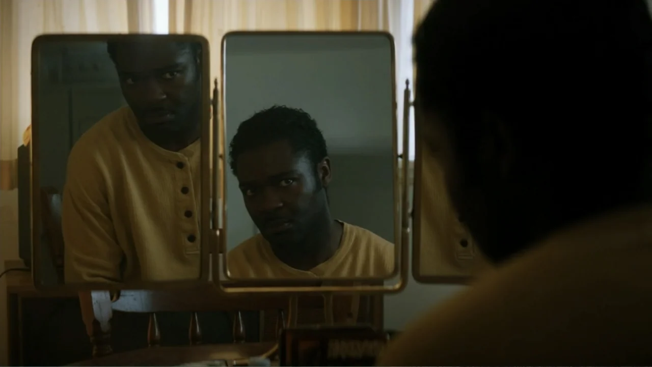 Nightingale (2014) movie still: medium — A man sits at a wooden vanity with a large tri-fold mirror setup. He examines his face intently while…