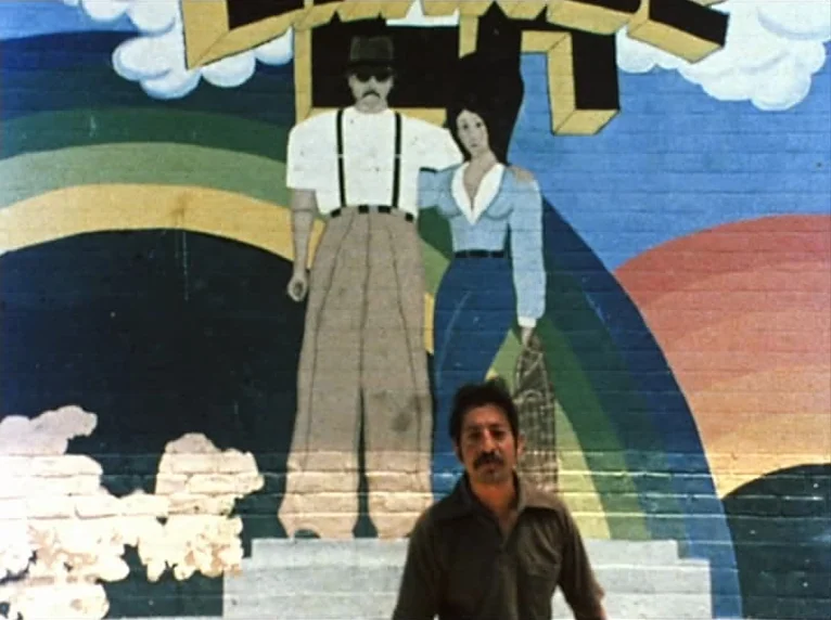 Mur Murs (1981) movie still: medium — A man stands before a vibrant, colorful mural painted on a brick wall. The mural depicts a stylized cartoon…