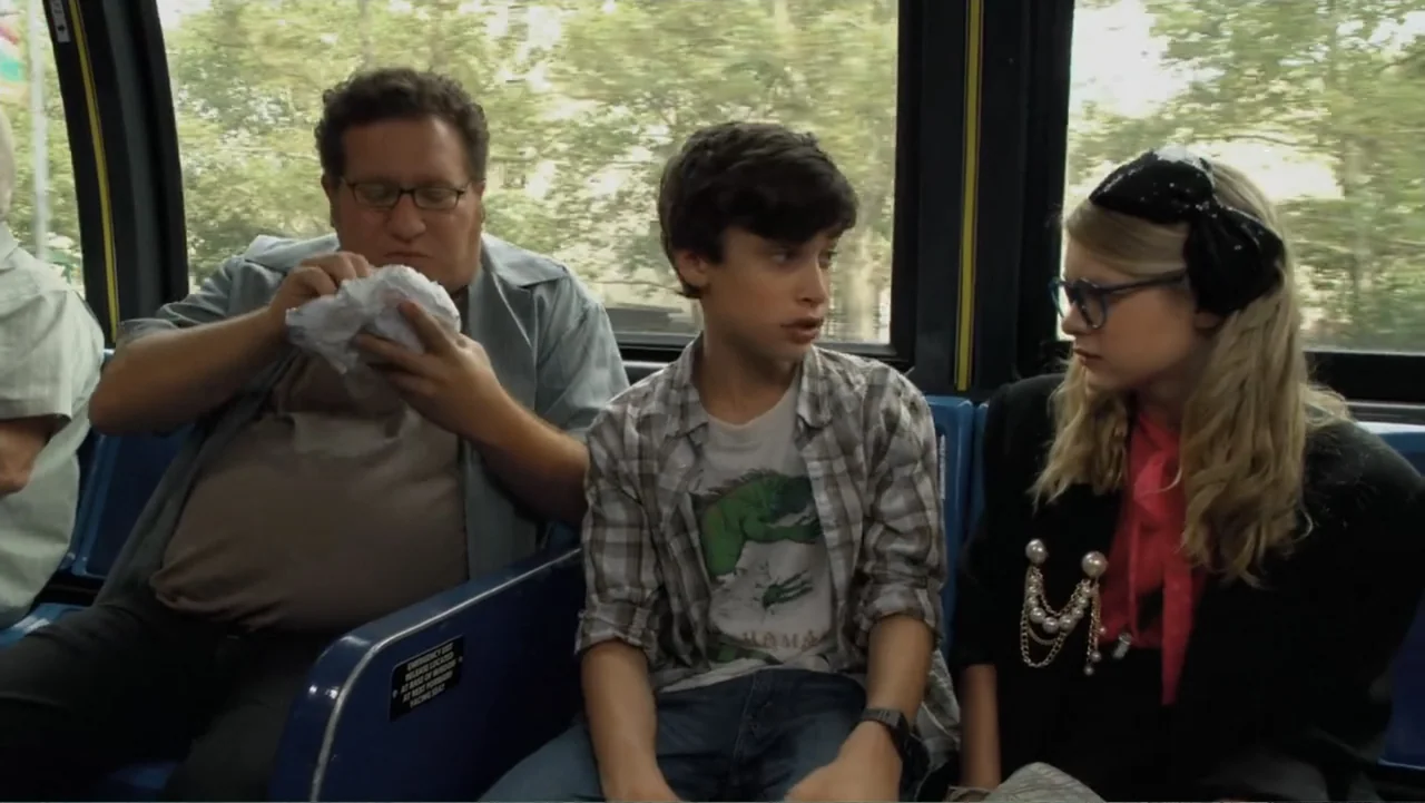 Jeremy Fink and the Meaning of Life (2012) movie still: medium — A crowded public transport bus interior with passengers sitting in blue plastic…