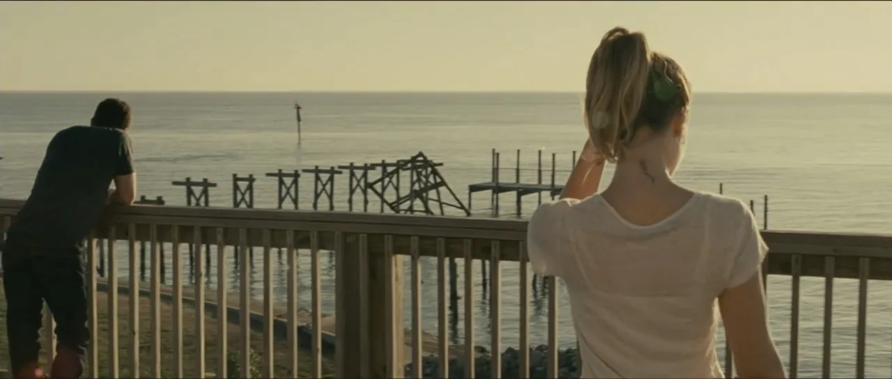 Contraband (2012) movie still: medium — A wooden observation deck overlooks a calm body of water with a decaying pier. A man and a woman stand by…