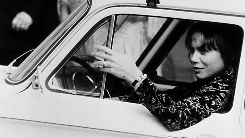 The Unbearable Lightness of Being (1988) movie still: medium — A woman sits in the driver seat of a light-colored vehicle with windows rolled down.…