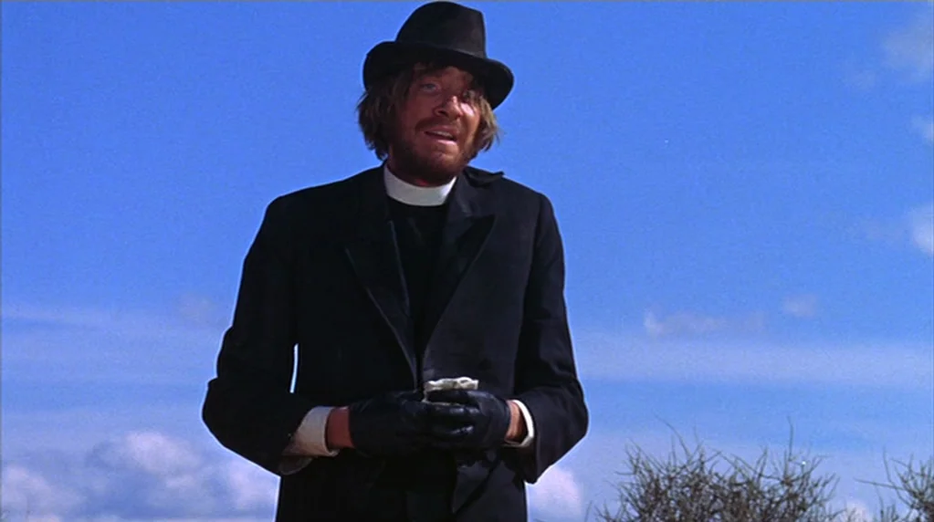 The Ballad of Cable Hogue (1970) movie still: medium — A man dressed as a priest stands outside against a vast, clear blue sky. He wears a black…
