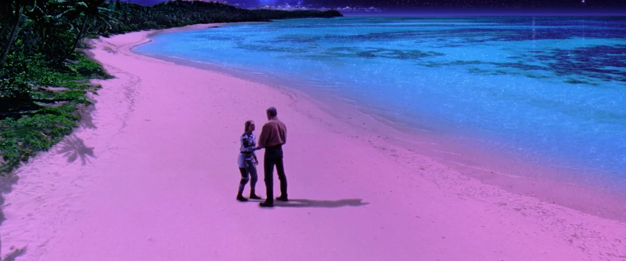 Contact (1997) movie still: wide — A wide beach at night with purple-tinted sand and vibrant blue ocean water. Two figures stand close together on…
