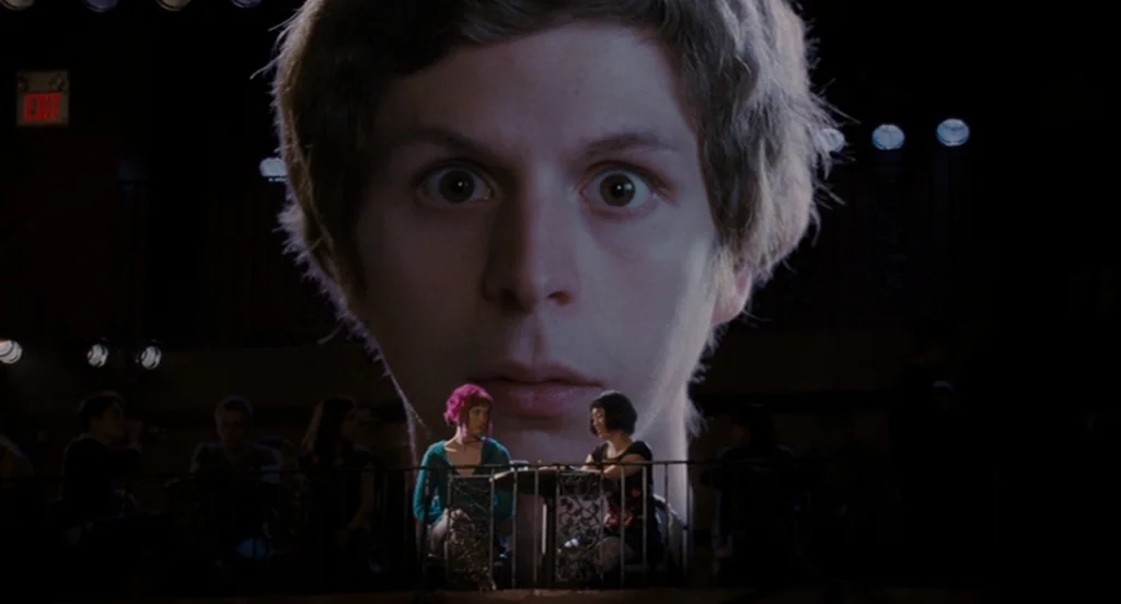 Scott Pilgrim Vs The World (2010) movie still: medium — Two women sit at a table inside a dark, shadowed music performance venue. A gargantuan…