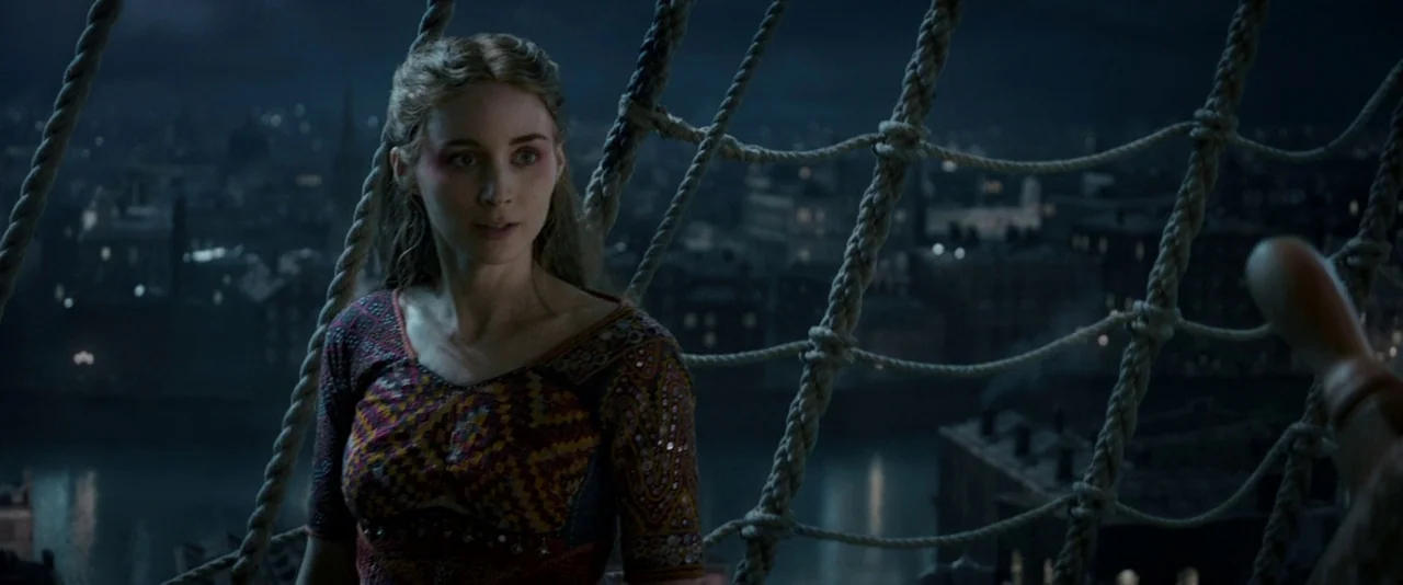 Pan (2015) movie still: medium — A woman stands atop the rigging of a sailing ship at night. Below her, the dark blurred lights of a city shoreline…