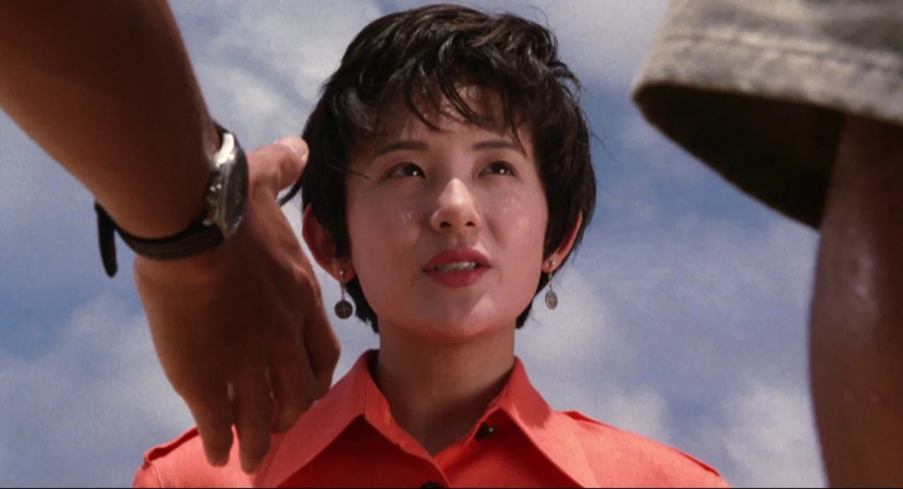 Godzilla vs. SpaceGodzilla (1994) movie still: closeup — A woman stands between two people under a bright sky. She looks directly forward while…