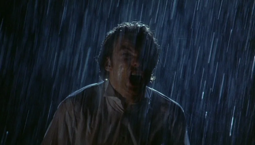 Edward II (1991) movie still: medium — A man stands outdoors at night under a downpour of heavy rain. The man looks forward with his mouth open…