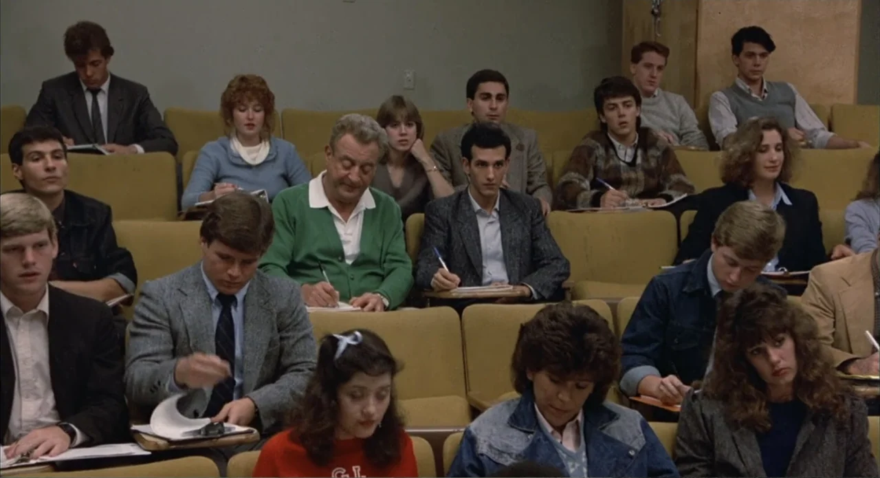 Back to School (1986) movie still: wide — A college lecture hall features rows of mustard-colored cushioned seats in a tiered arrangement. A group…