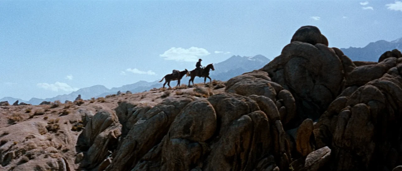 Comanche Station (1960) movie still: wide — An arid, rocky desert landscape stretches toward distant, pale blue mountains under a clear sky. A lone…