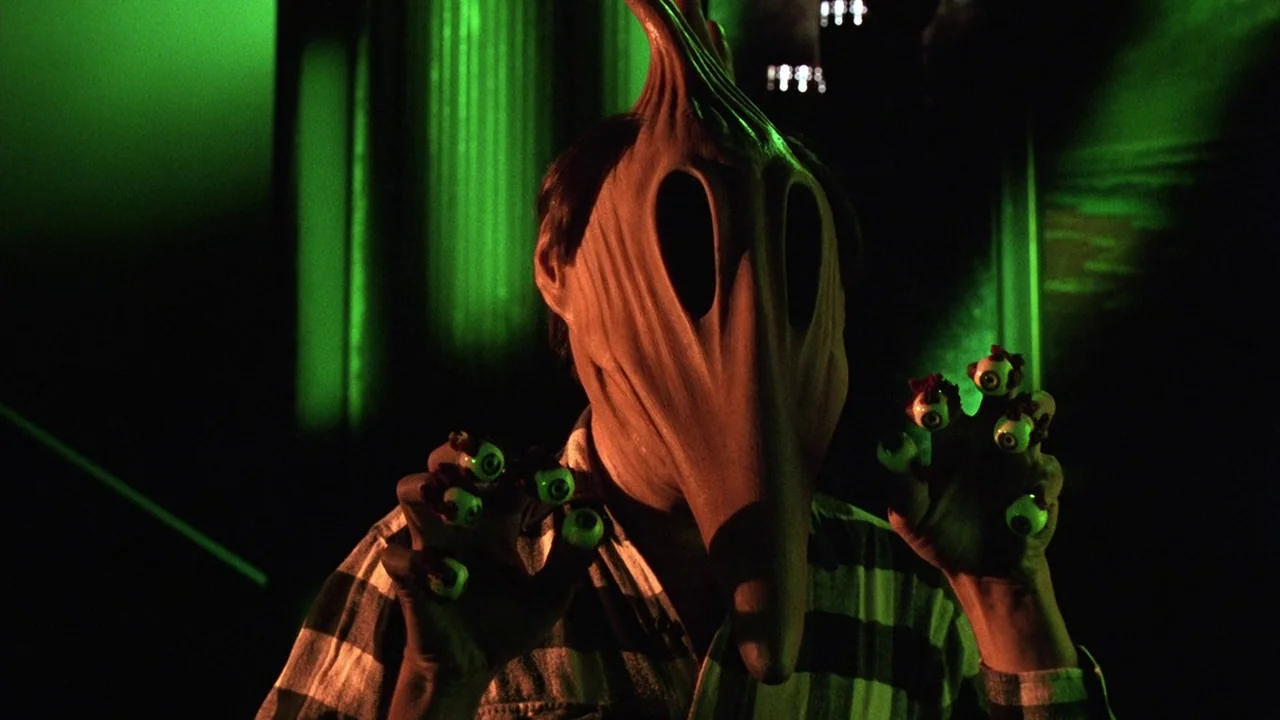 Beetlejuice (1988) movie still: medium — A figure stands in a dark environment illuminated by a harsh green light source. The subject wears a…