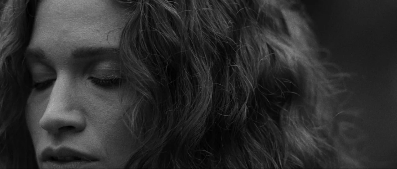 Braid (2018) movie still: closeup — An outdoor setting with natural lighting focusing on a person. The subject rests with eyes closed, highlighting…