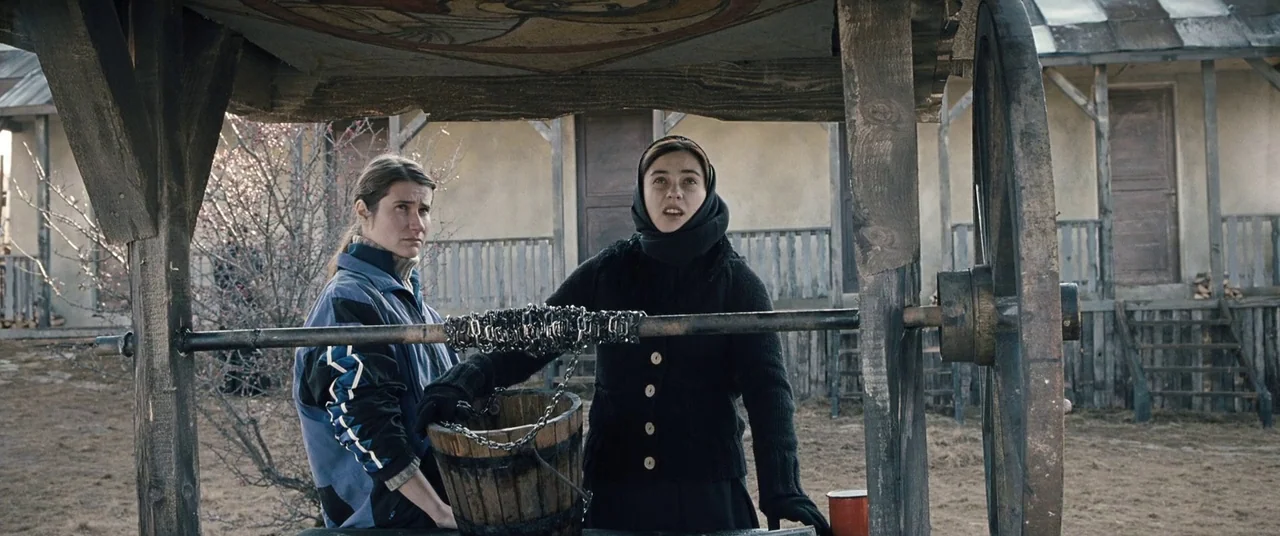 Beyond the Hills (2012) movie still: medium — An outdoor area with a wooden well structure under an overcast sky. Two women stand next to the well…