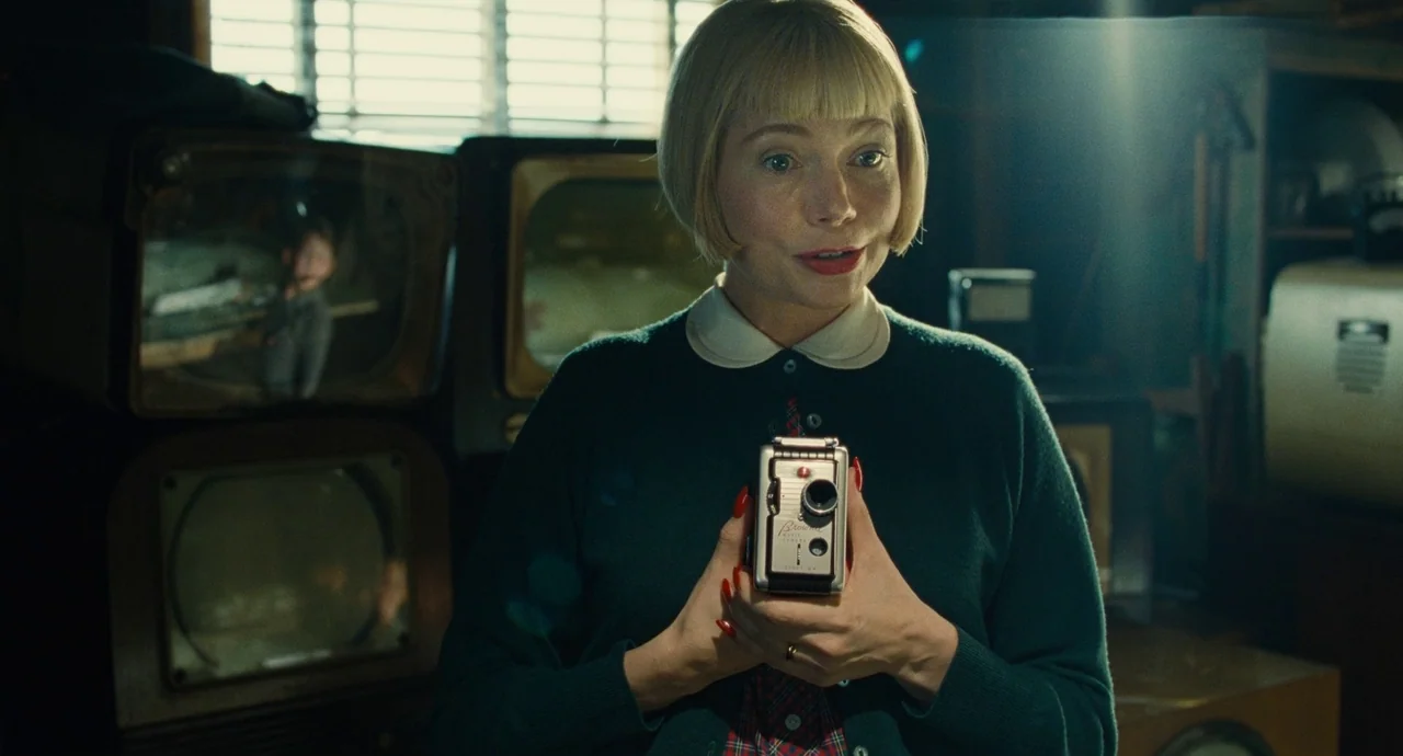 The Fabelmans (2022) movie still: medium — An interior storage room filled with vintage television sets and equipment. A woman holds a small metal…