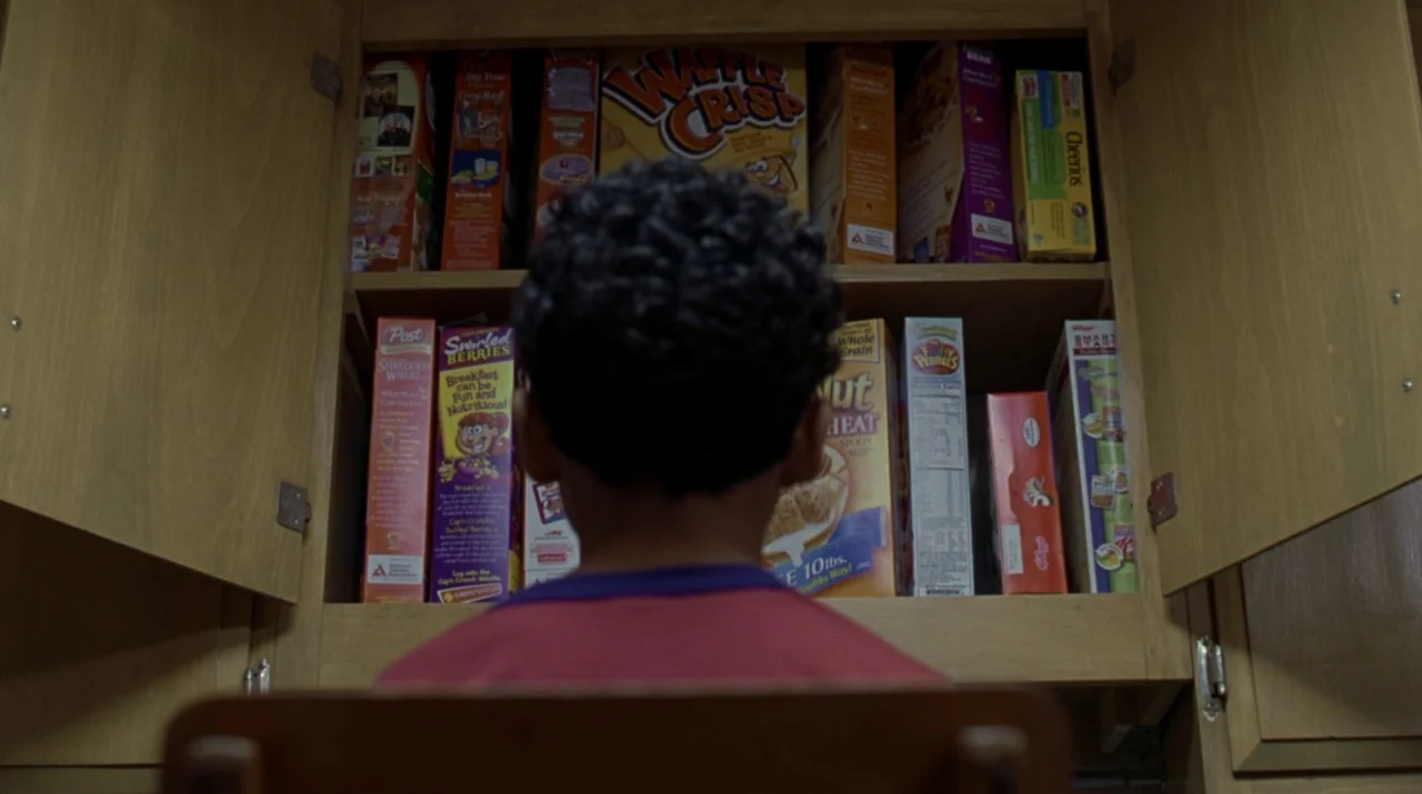 Lady in the Water (2006) movie still: medium — A wooden cabinet is filled with rows of assorted brand-name cereal boxes. A young child with curly…