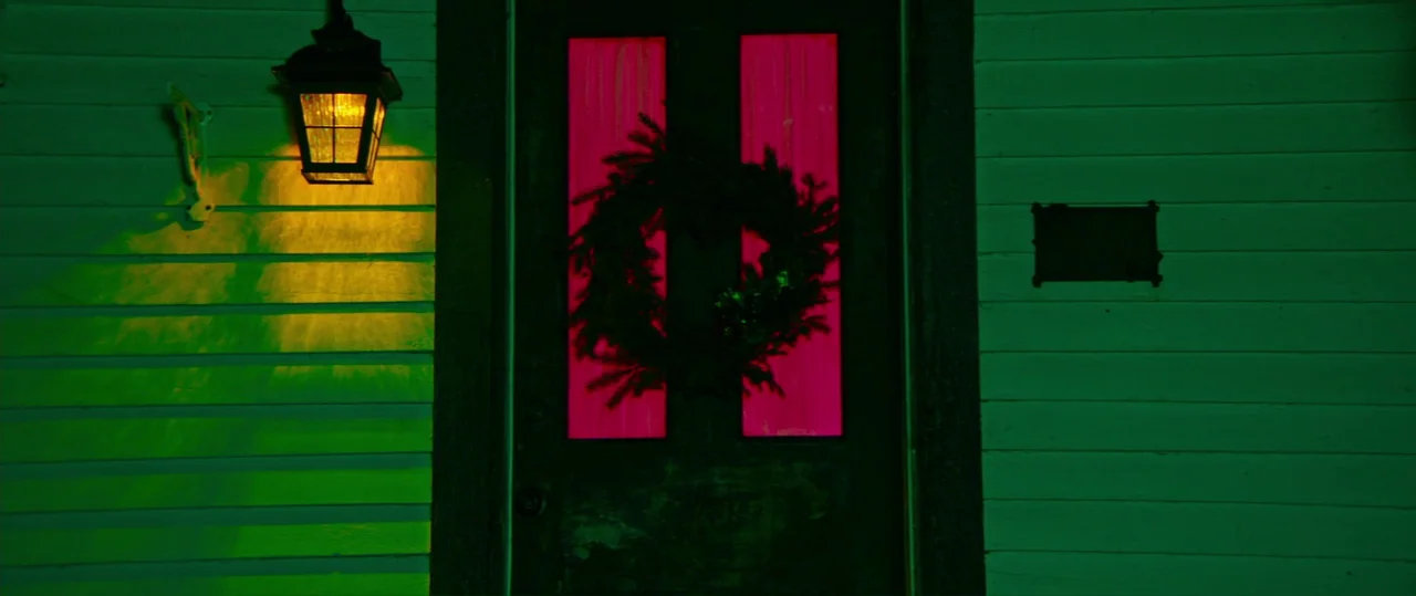 Random Acts of Violence (2019) movie still: medium — A dark wooden front door is centered on a wall covered in green horizontal siding. A wreath…