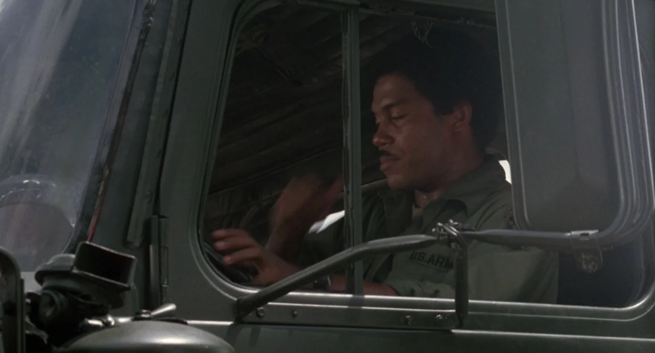 American Ninja (1985) movie still: medium — The interior cabin of an olive drab military truck is shown from outside. A man in a military uniform…