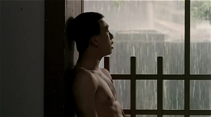 A Time To Love and A Time To Die (1985) movie still: medium — A man stands indoors next to a wood-framed window with glass panels. Heavy rain falls…