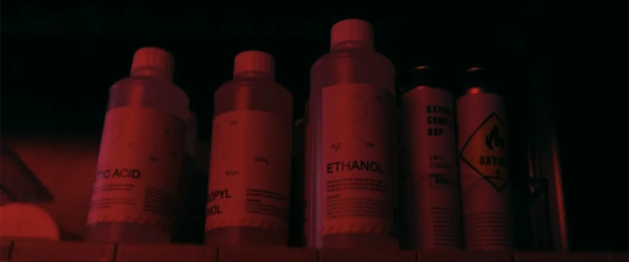 Ash (2025) movie still: closeup — A dark laboratory shelf holds several chemical bottles and oxygen canisters. The items are illuminated by a dim…