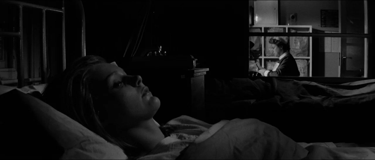 Bunny Lake Is Missing (1965) movie still: medium — A dimly lit room holds a woman resting in bed as a patient. A nurse works at a desk in a bright…