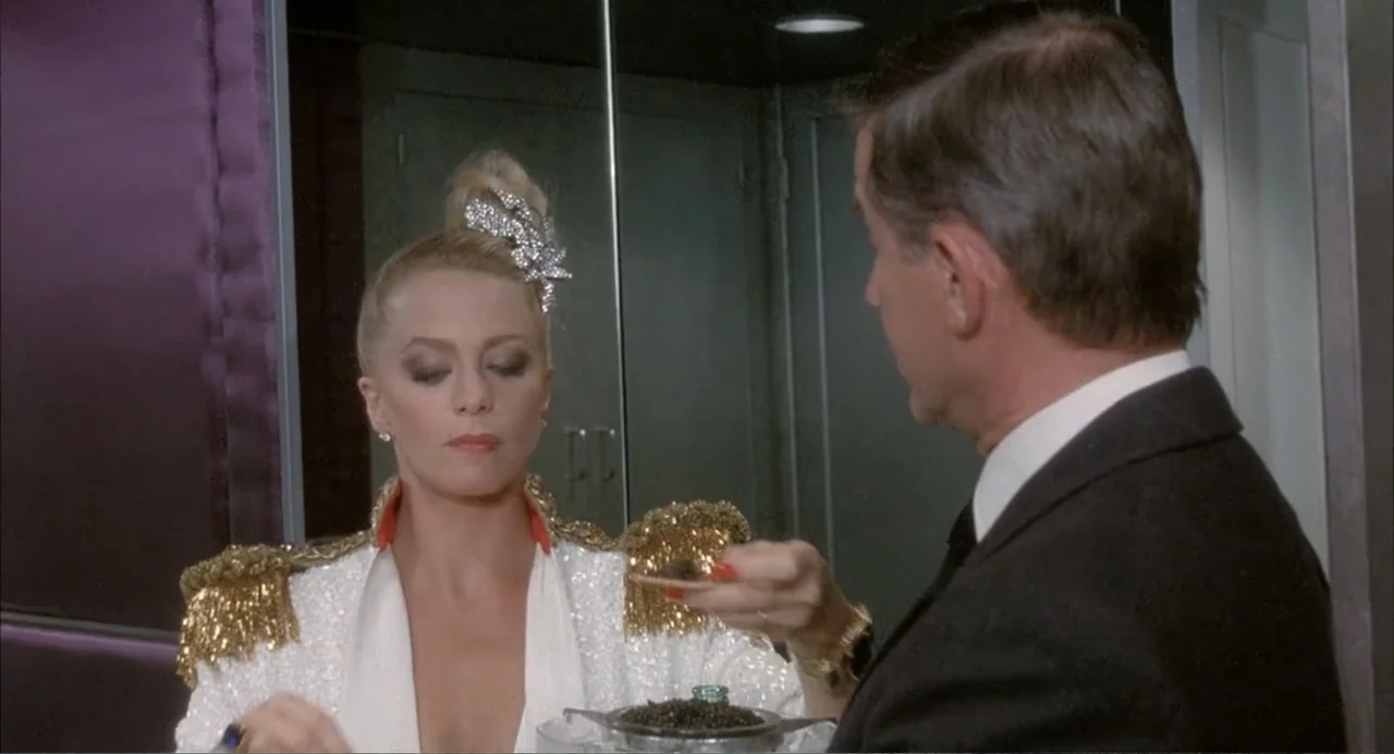Overboard (1987) movie still: medium — A dressing room features a dark purple partition wall and a mirror reflection. A woman in a sequined jacket…