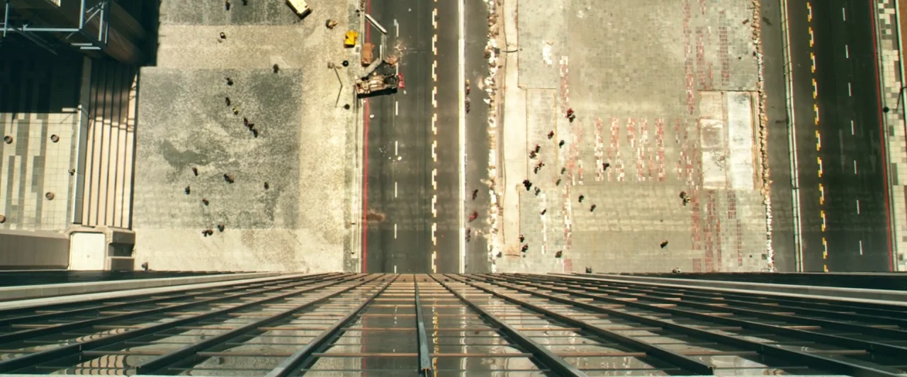 Dredd (2012) movie still: establishing — A top-down view looking down from the side of a tall glass building. People are tiny figures walking across…