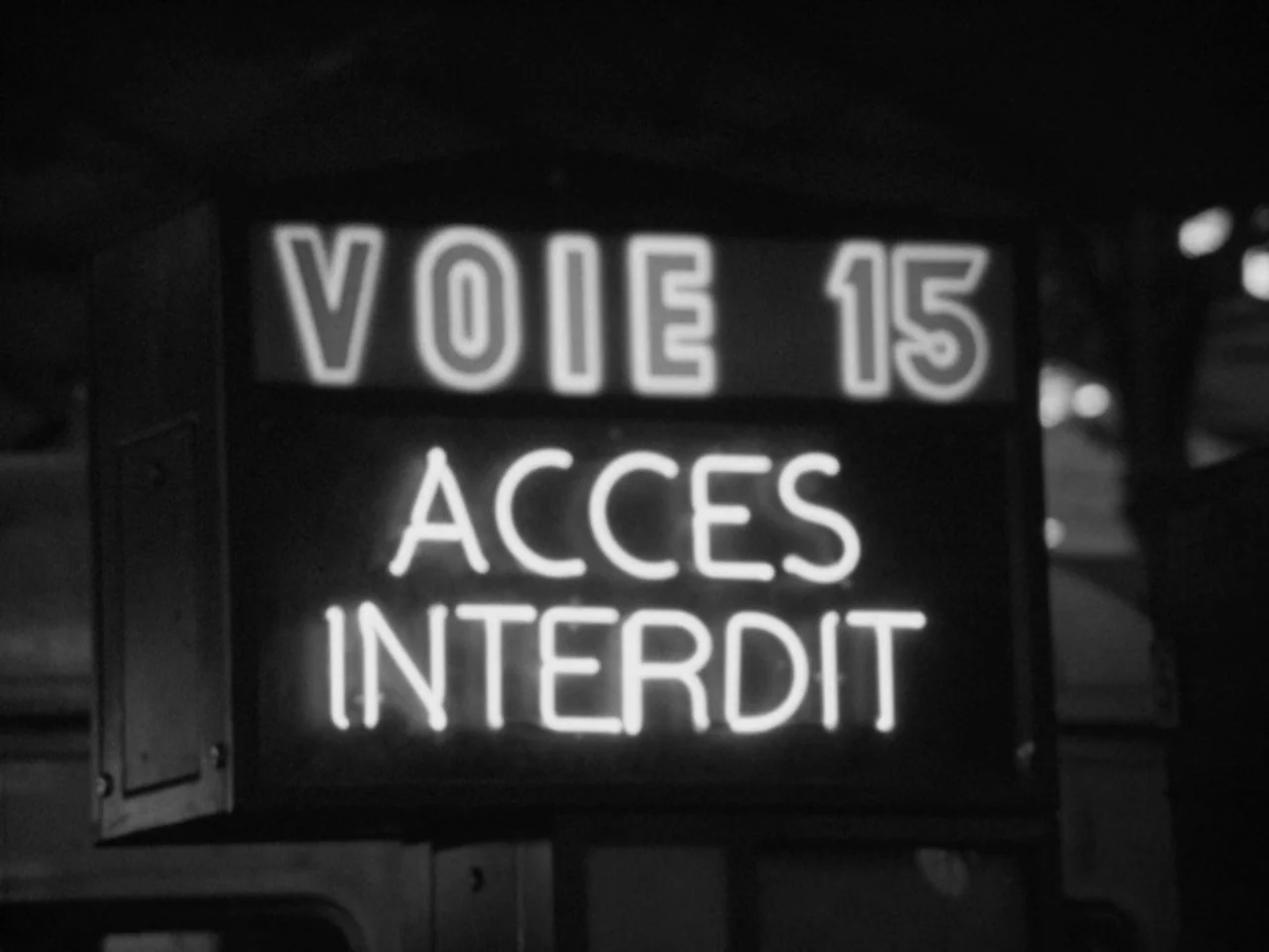 A Woman Kills (1968) movie still: closeup — An illuminated neon sign displays the French text VOIE 15 ACCES INTERDIT in darkness. The sign is…