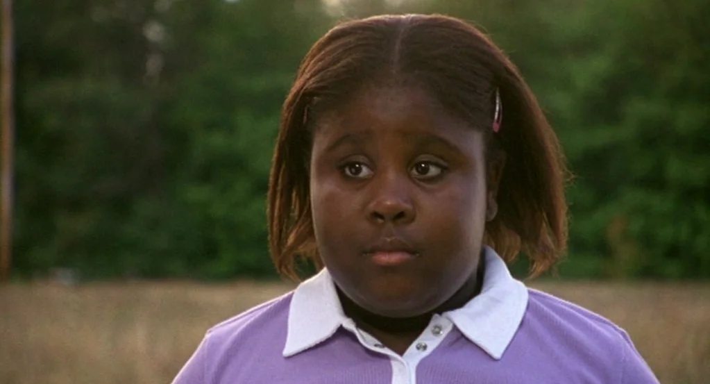 The Station Agent (2003) movie still: closeup — A grassy field with blurred green trees in the background during late afternoon. A young girl in a…