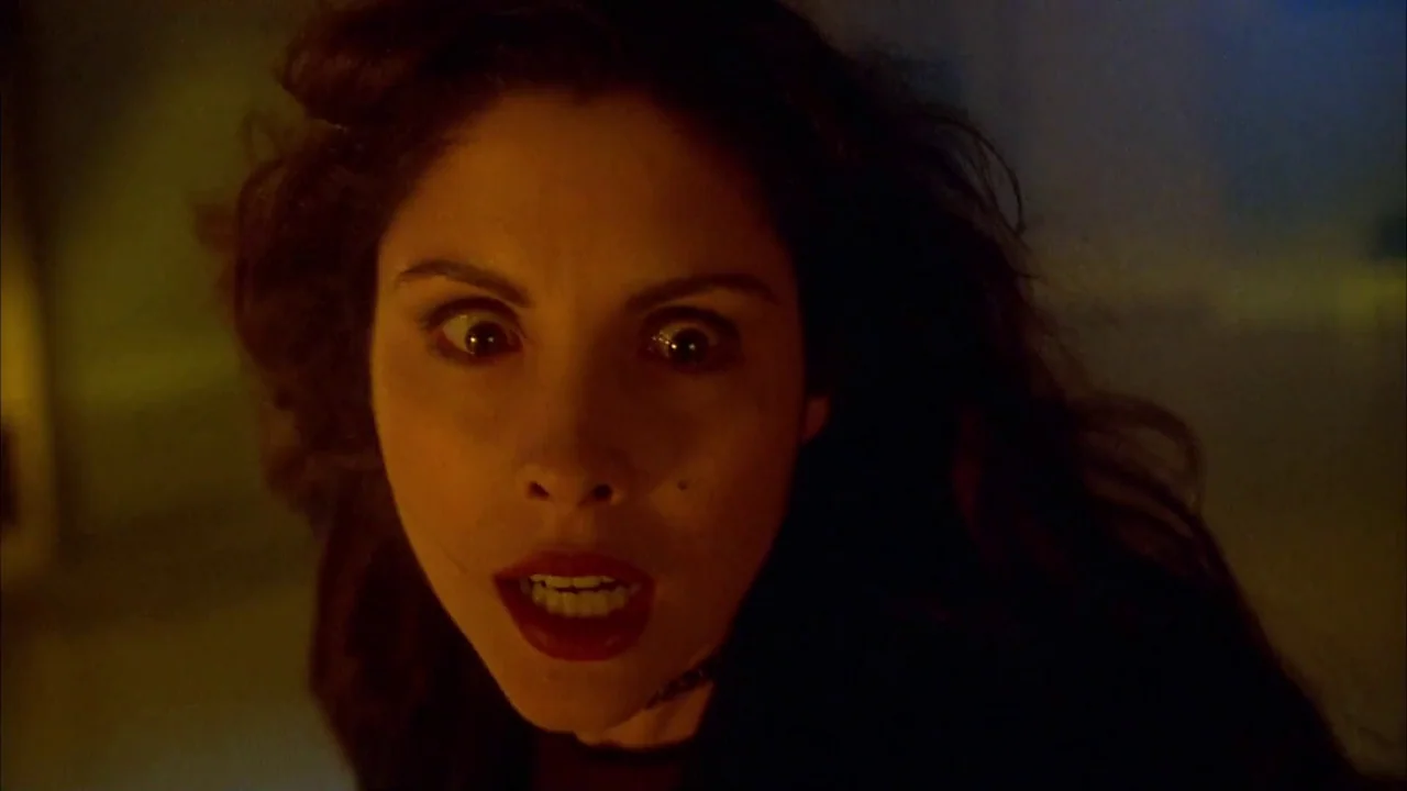 Hellraiser: Bloodline (1996) movie still: closeup — A dark indoor space with indistinct surroundings and warm, directional yellow light. A woman…