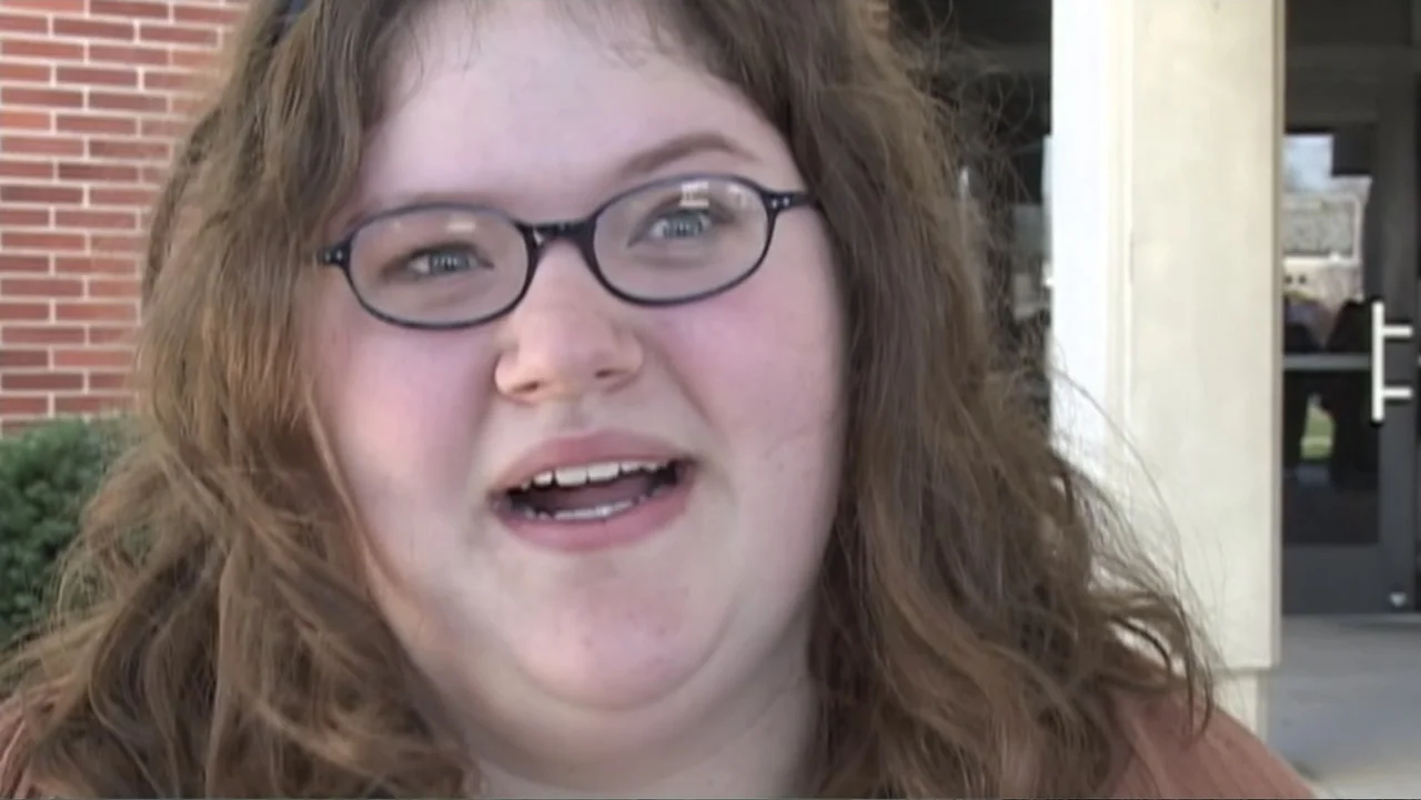 Super Size Me (2004) movie still: closeup — A teenager stands in front of a red brick school building. She is talking and looking directly toward…