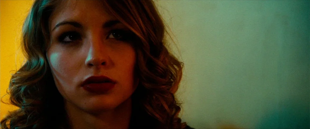 Hobo With A Shotgun (2011) movie still: closeup — A close-up shot focuses on a woman inside a dimly lit interior space. The subject looks directly…