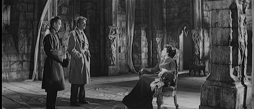 I Vampiri (1957) movie still: wide — A spacious stone chamber with high ceilings and heavy columns features rough-hewn architecture. Two men wearing…