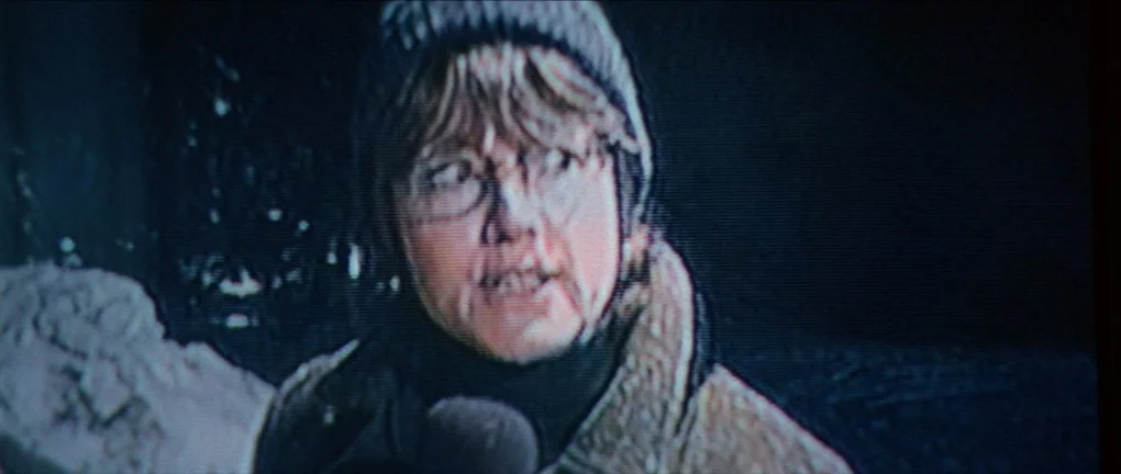 The Pledge (2001) movie still: medium — A person stands outside at night with a large mound of snow nearby. The subject speaks into a microphone…
