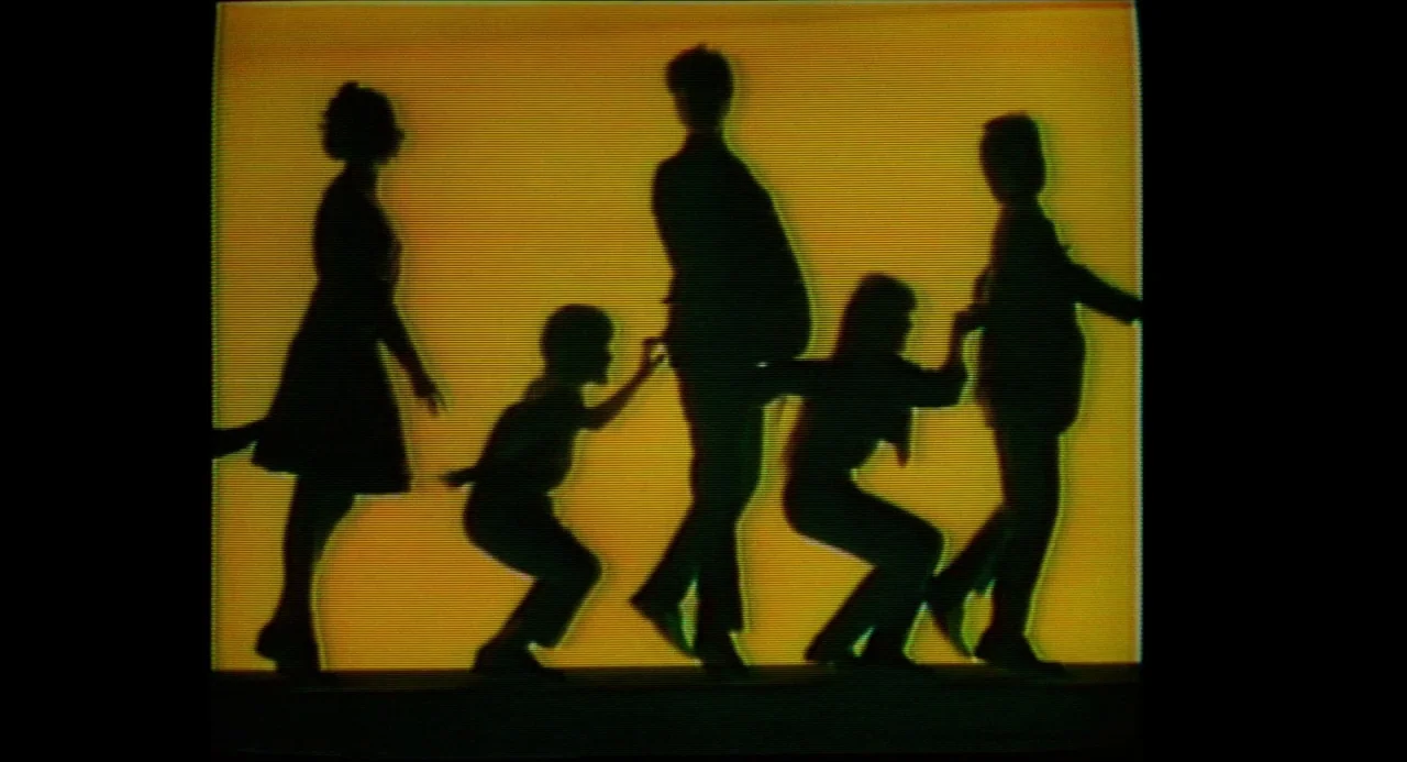 True Stories (1986) movie still: wide — A group of five figures in silhouette moves across a solid vibrant yellow screen. The VHS texture creates…