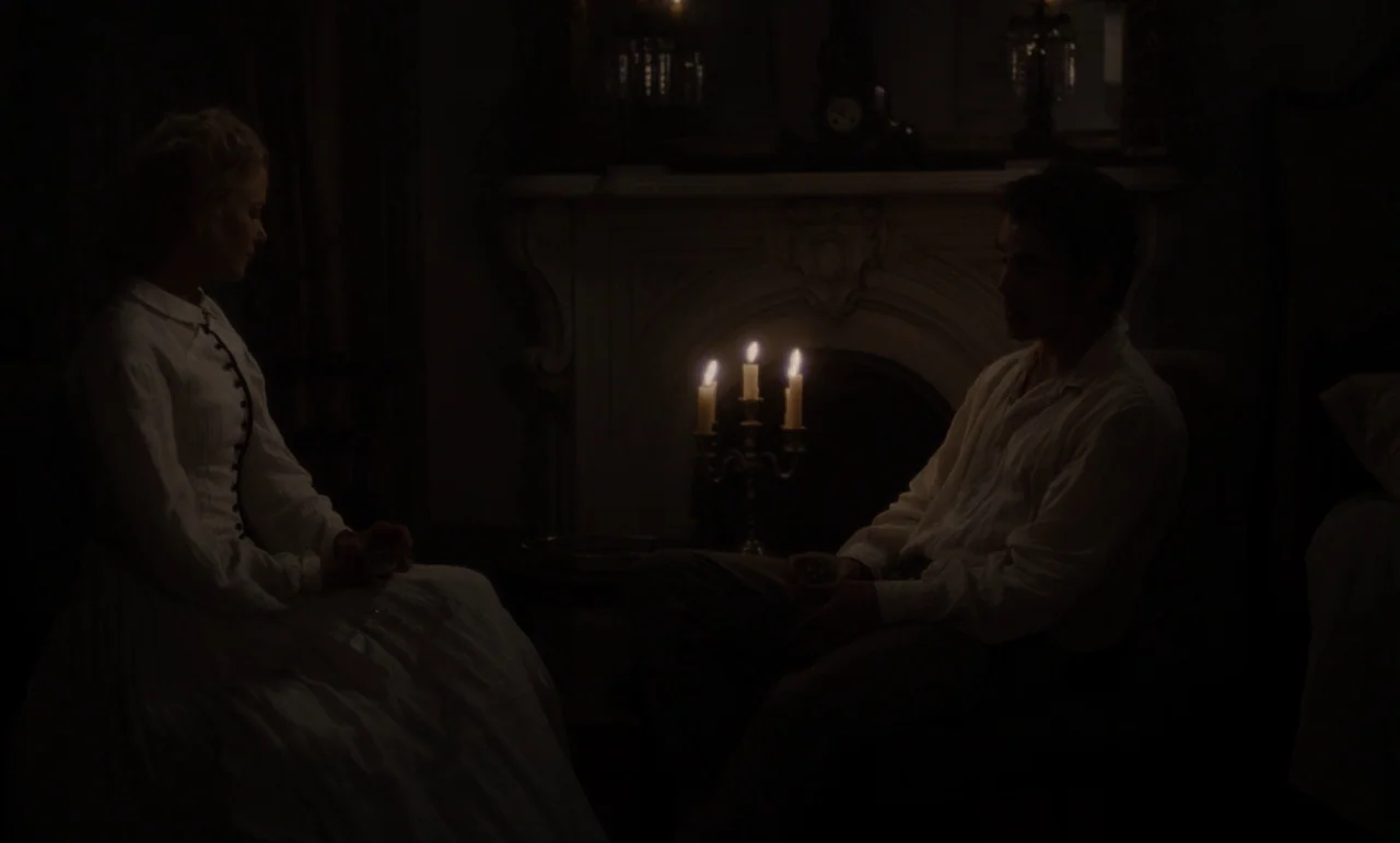 The Beguiled (2017) (2017) movie still: medium — A dark parlor features a large stone fireplace mantel behind a lit three-wick candelabra. A woman…