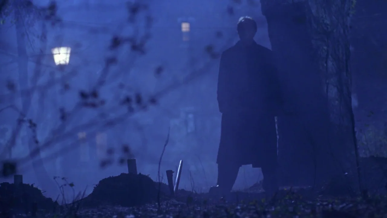 Hellraiser: Hellworld (2005) movie still: fullbody — A dark night park with a lone tree and a visible streetlamp in distance. A man in a long coat…