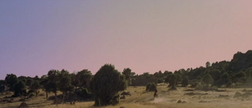 Django Kill (1967) movie still: establishing — A dry, hilly field is sparsely covered in low-lying green shrubs and rocks. A lone horseman rides…