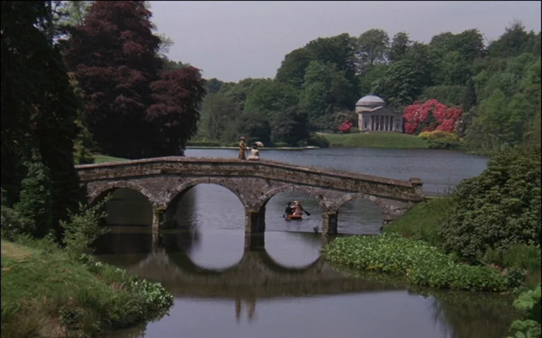 Barry Lyndon (1975) movie still: wide — A classic English landscape park with a multi-arched stone bridge spanning a tranquil lake. A classical…