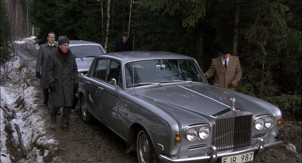 Gorky Park (1983) movie still: medium — A narrow dirt trail runs through a dense pine forest with patches of snow. Four men in formal coats and…