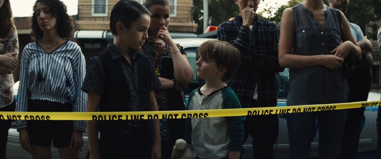 Daniel Isn’t Real movie still: medium — A group of people stands behind a length of bright yellow police caution tape. The individuals are…