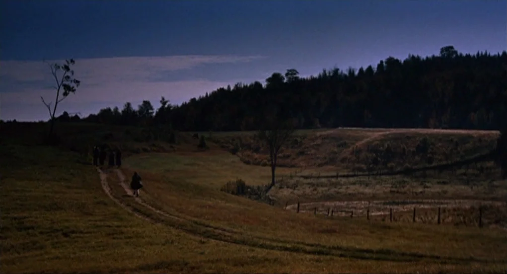 The Trouble With Harry (1955) movie still: wide — An expansive rural field with rolling hills at dusk under a deep blue sky. A small group of…