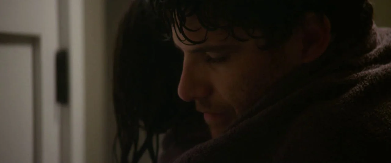 Night Owls (2015) movie still: closeup — An interior space contains a person partially obscured by a doorway frame. A man with damp hair holds…